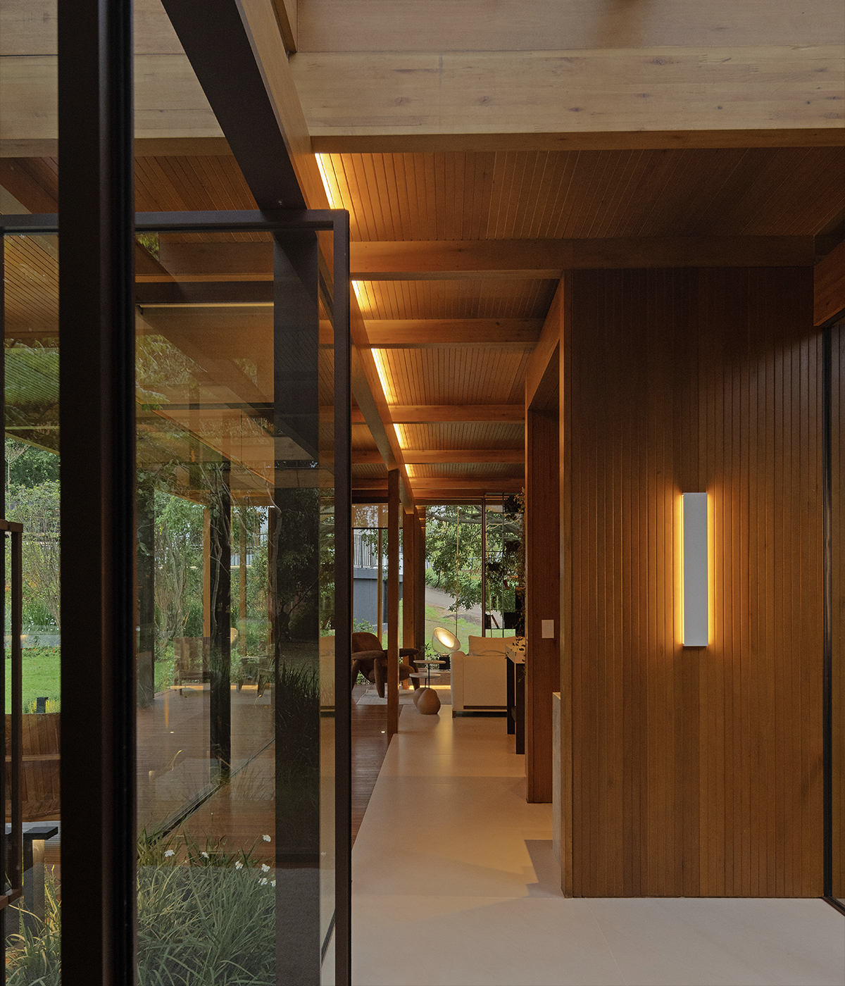 This photo features, in the foreground on the right, a white-finished Reflex wall light by Stella, turned on with lateral beams. The product is installed on a red varnished wooden wall that f