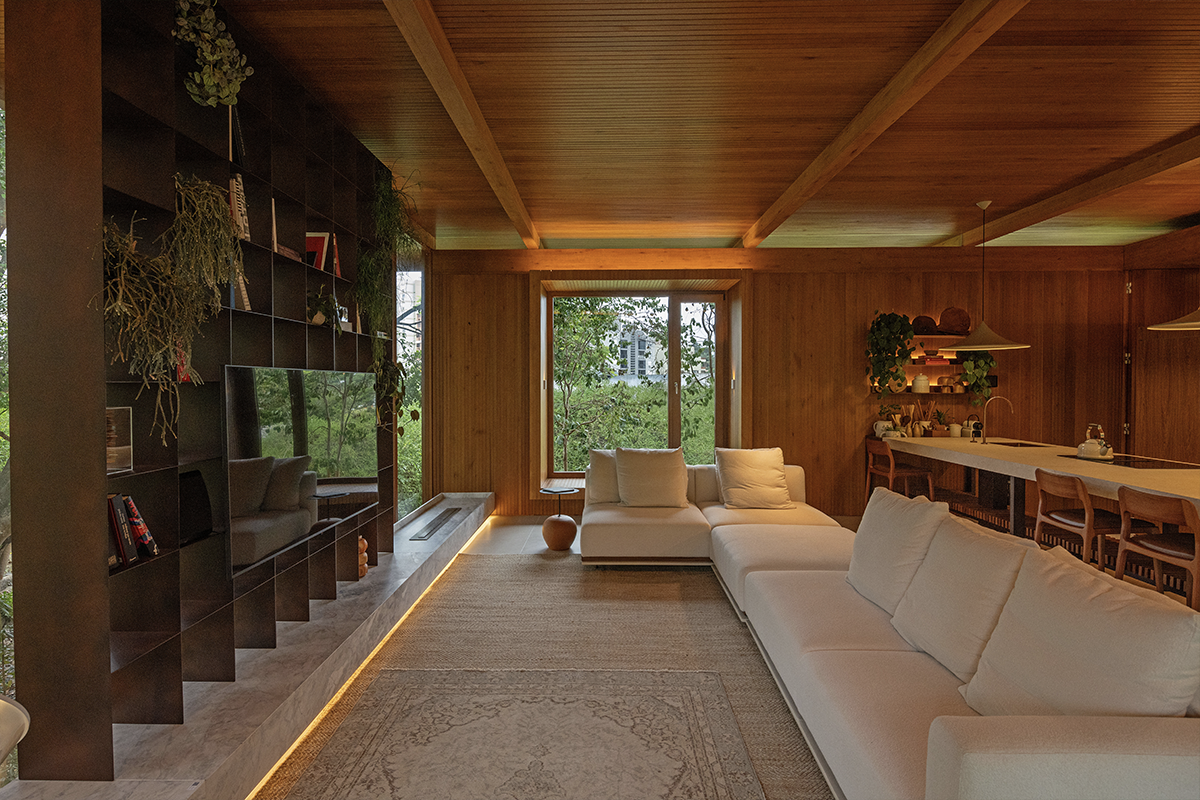 The image shows a living room with a large white sofa in front of a TV panel with book and plant niches. A large stone with an embedded ledge runs the entire lower section of the panel, featu