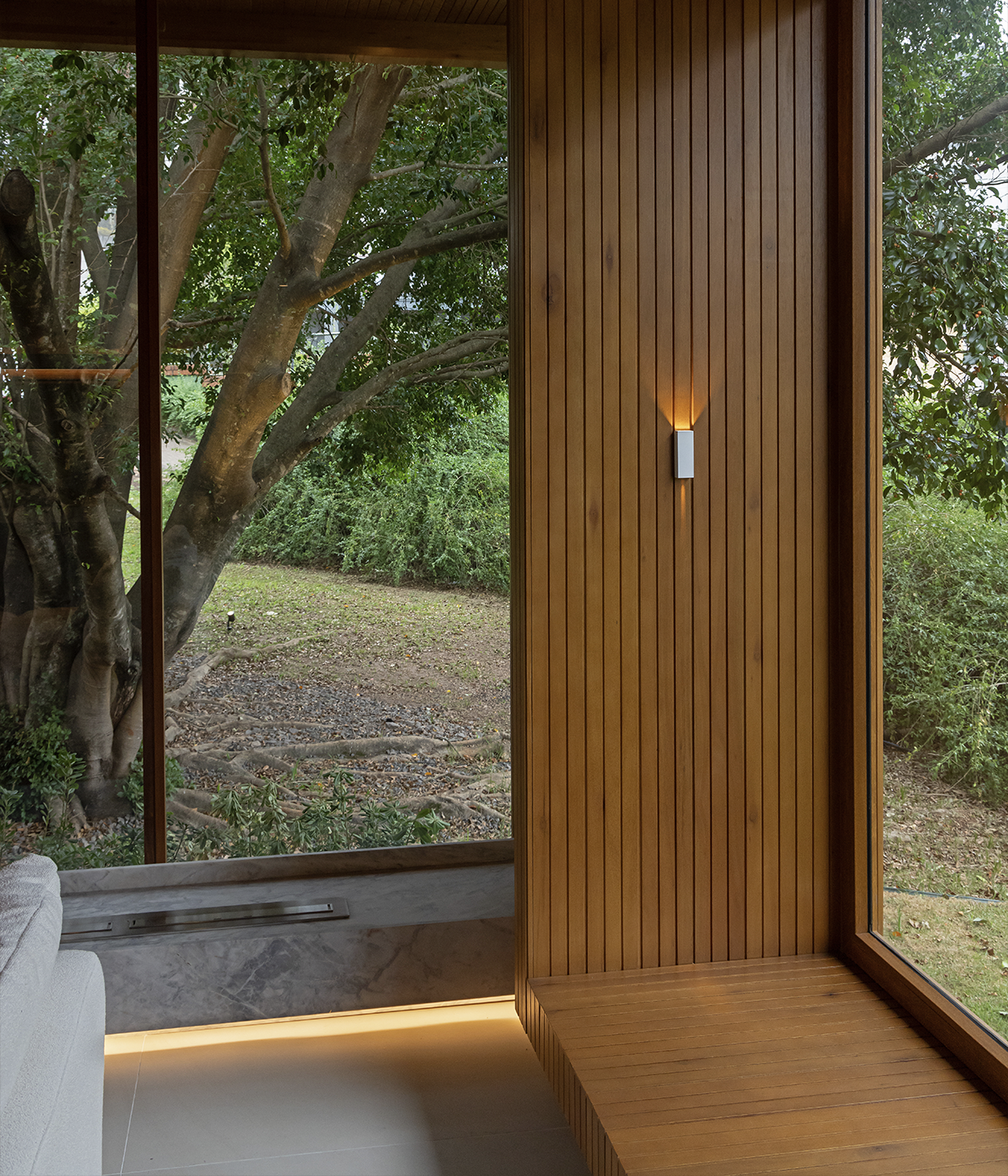 A window projected outward in a bay window style reveals the surrounding nature. On the side of the wooden structure, a Wall Mini wall light has a 90º open beam at the top and a 4º narrow bea